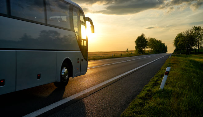 White Bus driving along the asphalt road at sunset.